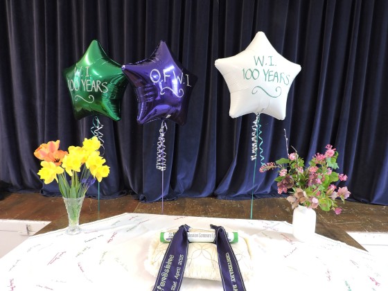 the Centenary Baton with celebratory balloons, flowers and Barford St. Michael's tablecloth at the Village hall